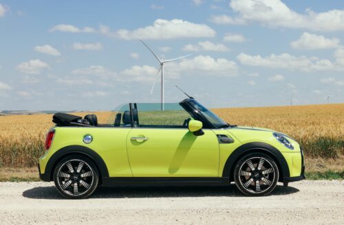 Mini cabriolet jaune garée devant un champs de blé, capote ouverte
