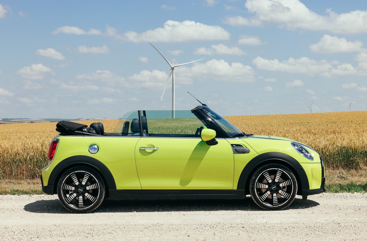 Mini cabriolet jaune garée devant un champs de blé, capote ouverte