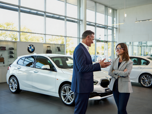 Conseiller BMW en discussion avec une cliente dans une concession moderne, devant une BMW Série 1 blanche, illustrant la qualité de la relation client et du service premium BMW Equation à Toulouse.